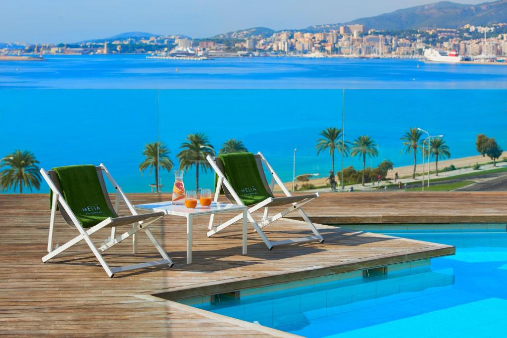 马略卡岛帕尔马帕尔马湾梅利亚酒店的游泳池畔的甲板上配有两把椅子和一张桌子
