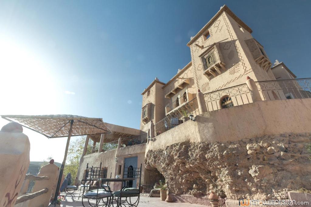 凯拉Kasbah Agoulzi古堡旅馆的一座配有桌椅和遮阳伞的建筑