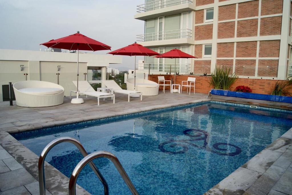 瓜达拉哈拉天鹅绒广场酒店的一座带椅子和遮阳伞的游泳池位于一座建筑旁边