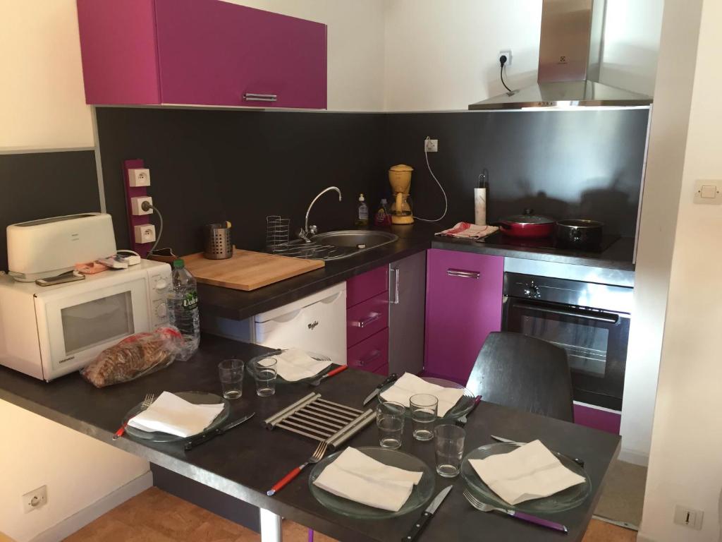 巴涅尔-德吕雄Appartement Duplex的厨房配有紫色橱柜和带微波炉的桌子