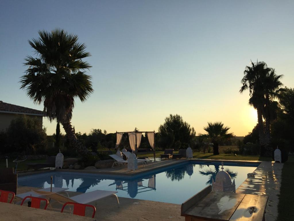 佩皮尼昂Escapades Lointaines的一个带椅子和棕榈树的游泳池,并可欣赏日落美景