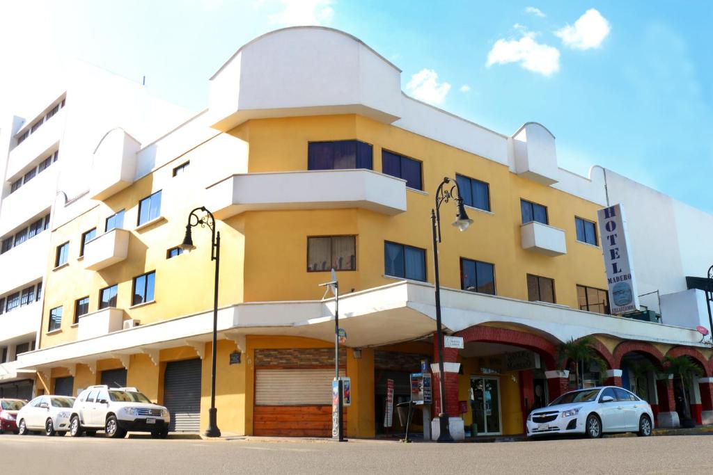 比亚埃尔莫萨Hotel Madero的一座黄色的建筑,前面有汽车停放