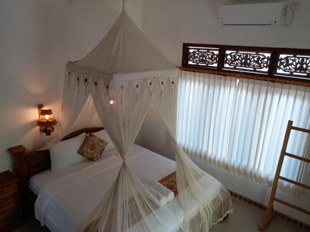 乌布帕恩迪家庭旅馆的卧室配有带白色窗帘的天蓬床