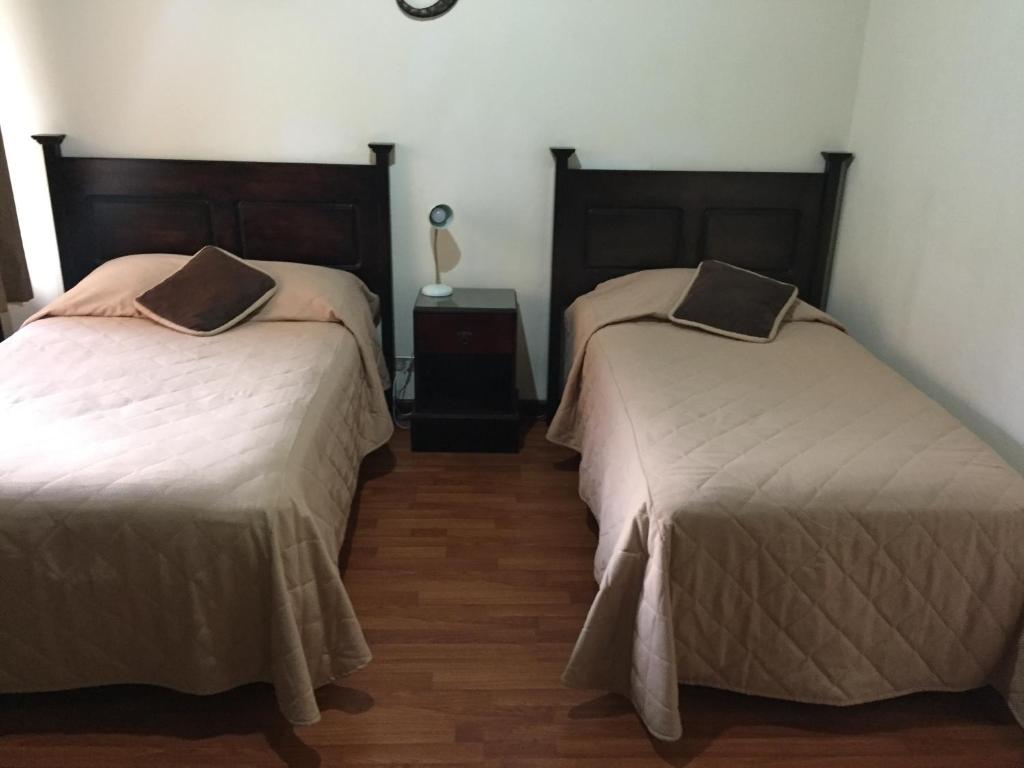 危地马拉康福特旅舍的一间卧室配有两张床和一张带台灯的桌子