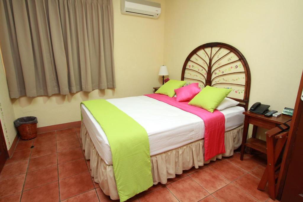 马那瓜Hotel Colibri的一间卧室配有带绿色和粉红色枕头的床