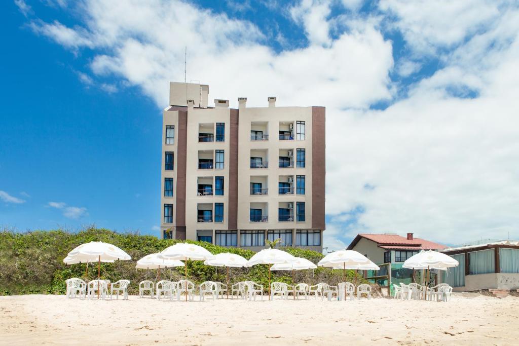 弗洛里亚诺波利斯棕榈滩公寓式酒店的海滩上一座带白色椅子和遮阳伞的建筑