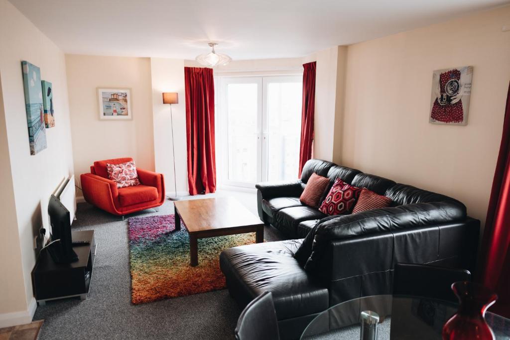 贝尔法斯特Comfortable Belfast city centre apartment的客厅配有黑色真皮沙发和红色椅子