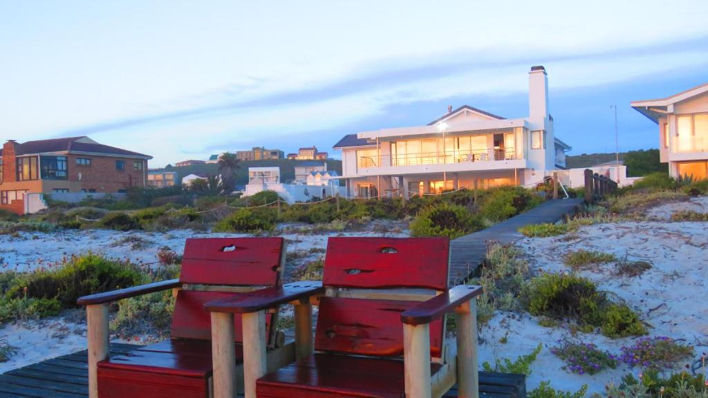 伊泽芳登On The Beach Apartments的两把红色椅子坐在房子旁边的木板路上