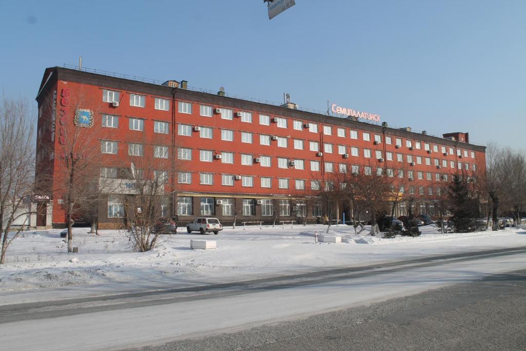 塞米伊Semey Hotel的街道前的雪地里一座大型红色建筑