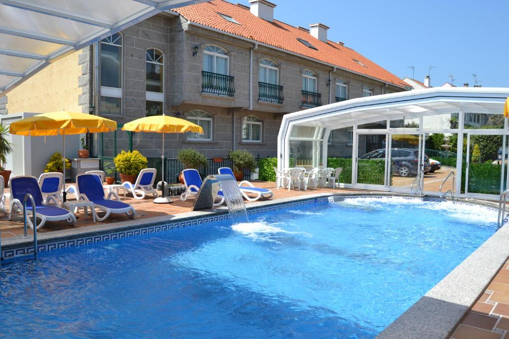 维拉加尔西亚·德·阿劳萨普拉亚孔波斯特拉酒店的一座带椅子和遮阳伞的游泳池位于一座建筑旁边