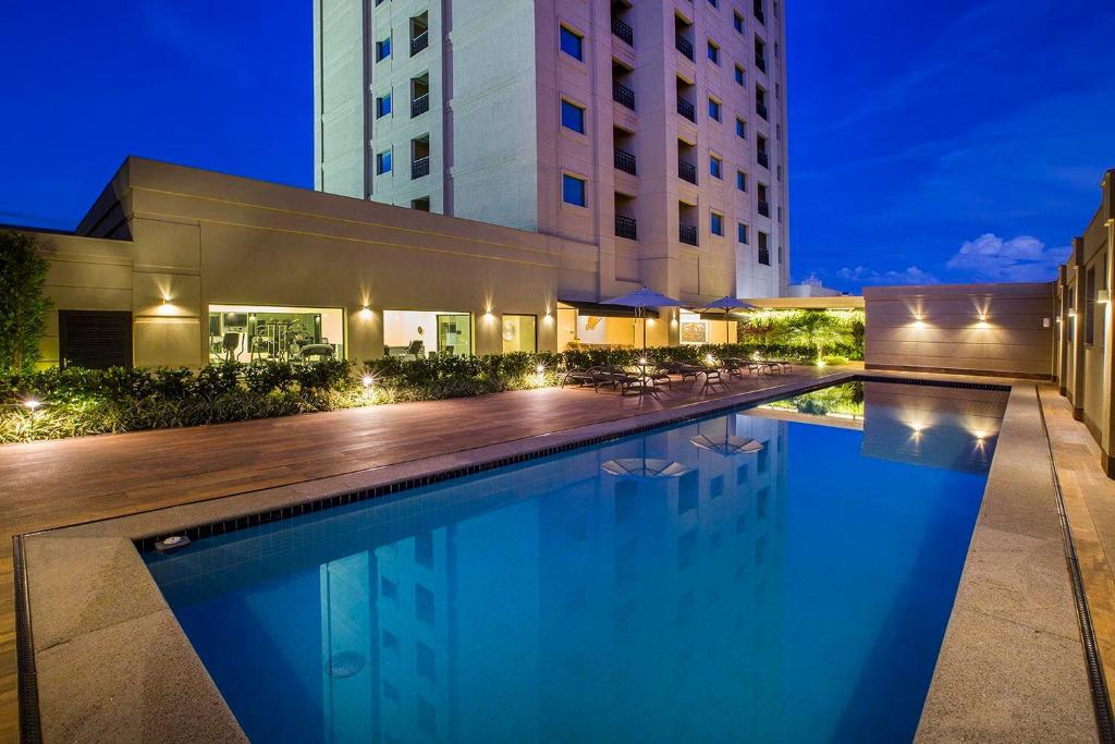 阿拉拉夸拉Hotel Araucaria Flat的一座游泳池,在晚上在建筑物前