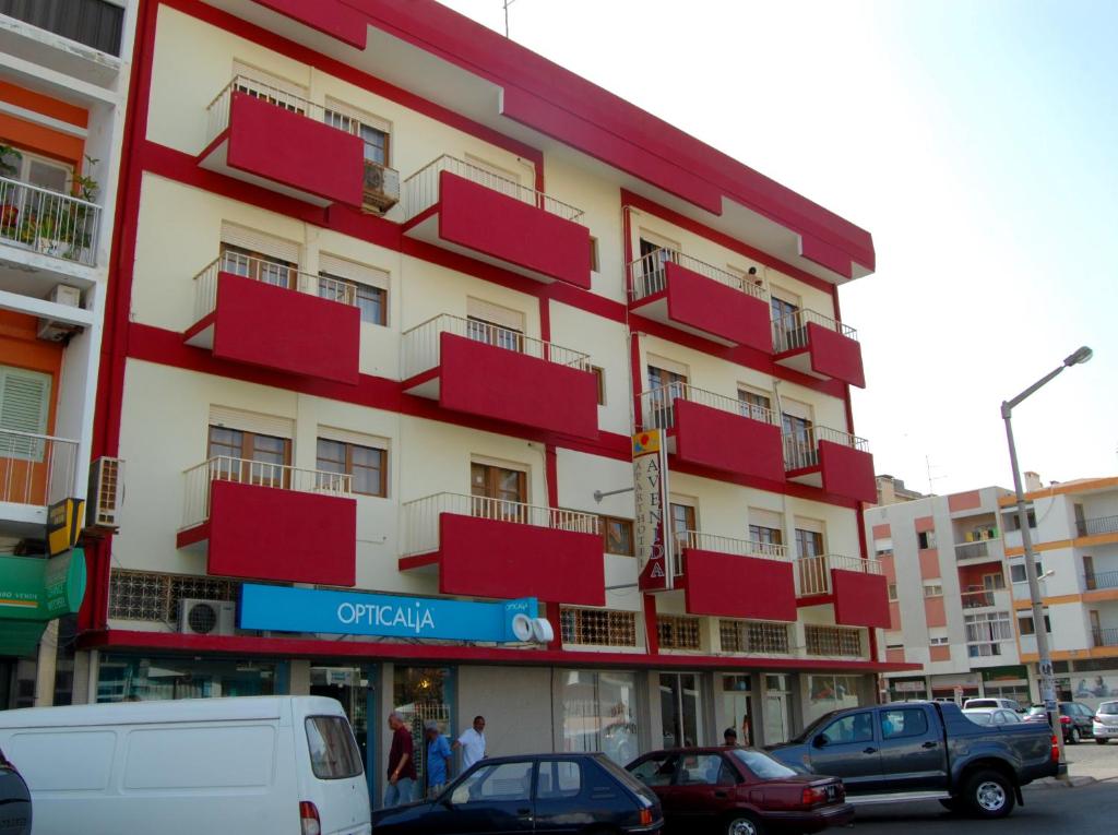 明德卢Aparthotel Avenida的一座红色和白色的建筑,前面有汽车停放