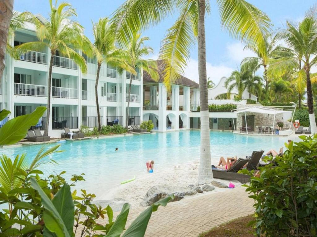 道格拉斯港Beach Club Port Douglas Luxury Apartments的棕榈树的度假泳池和泳池内的人