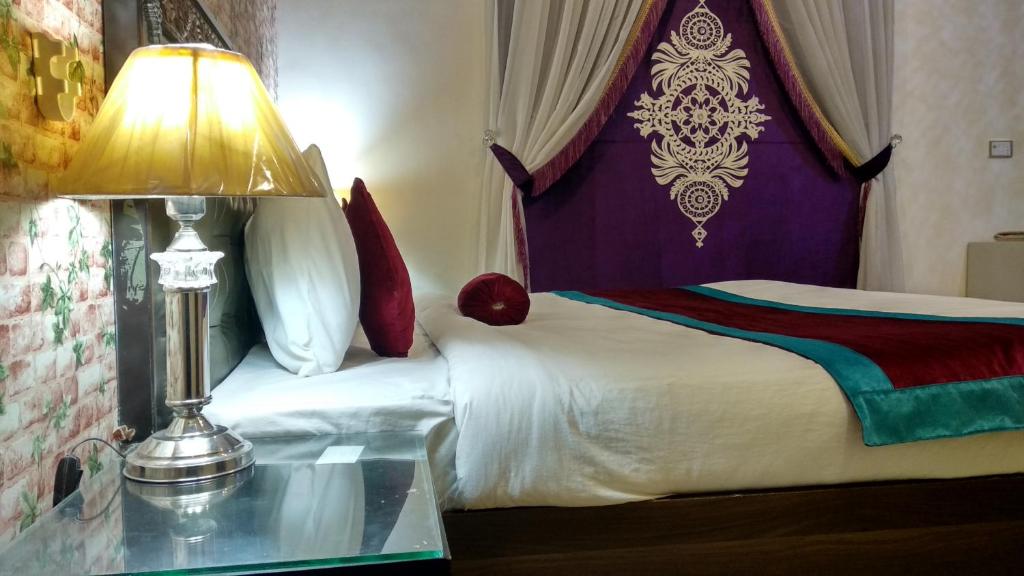 拉合尔Rose Palace Hotel, Garden Town的一间卧室配有一张床和一张带台灯的桌子