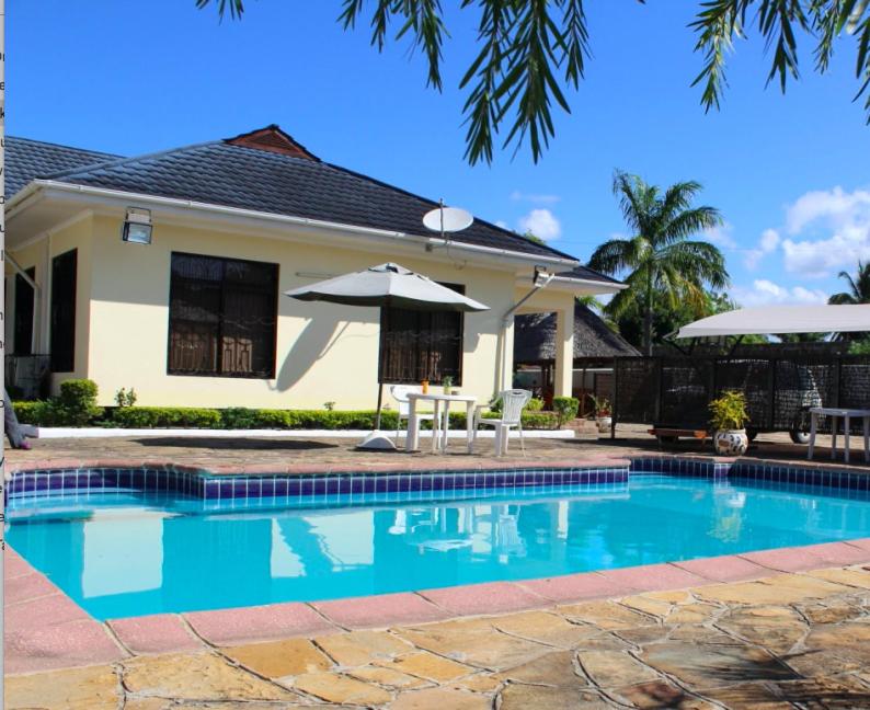 巴加莫约IDC Guest House的一个带遮阳伞和房子的游泳池