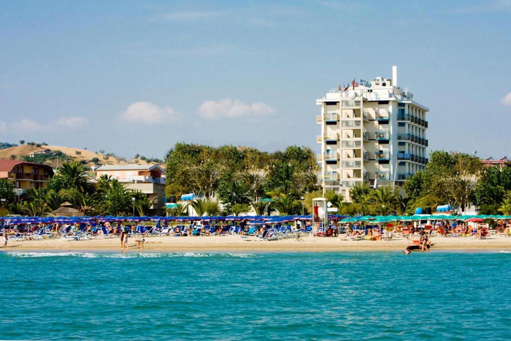 阿尔巴·阿德里亚蒂卡Hotel Excelsior的一片带人与遮阳伞的海滩和一座建筑