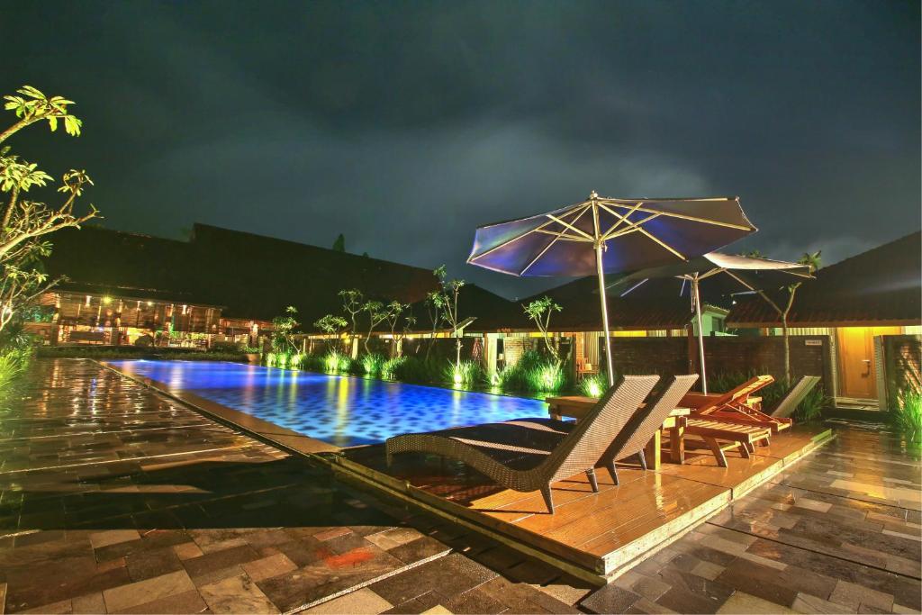 婆罗浮屠婆罗浮屠商羯罗酒店的夜间带椅子和遮阳伞的游泳池