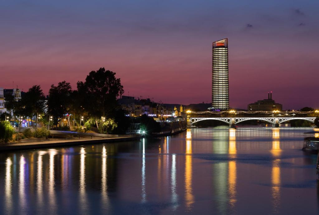 塞维利亚塞维利亚托雷欧洲之星酒店的一座河上的桥梁,晚上有一座建筑
