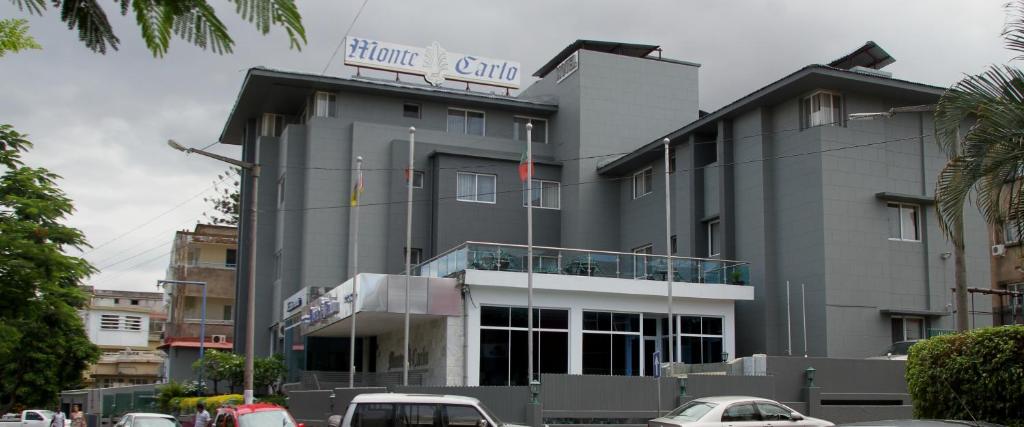 马普托Hotel Monte Carlo的一座灰色的大建筑,前面有汽车停放