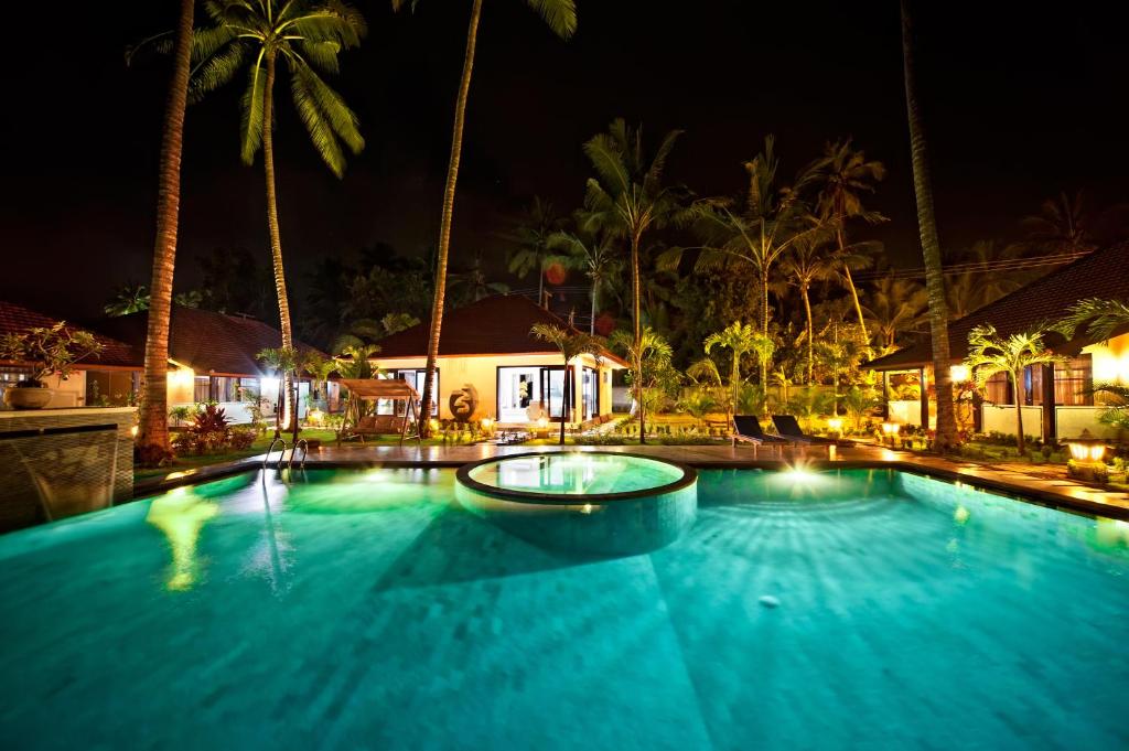 甘地达萨Rossa Garden Hotel的棕榈树的夜间大型游泳池