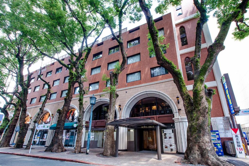熊本奥库斯酒店的前面有树木的大型砖砌建筑