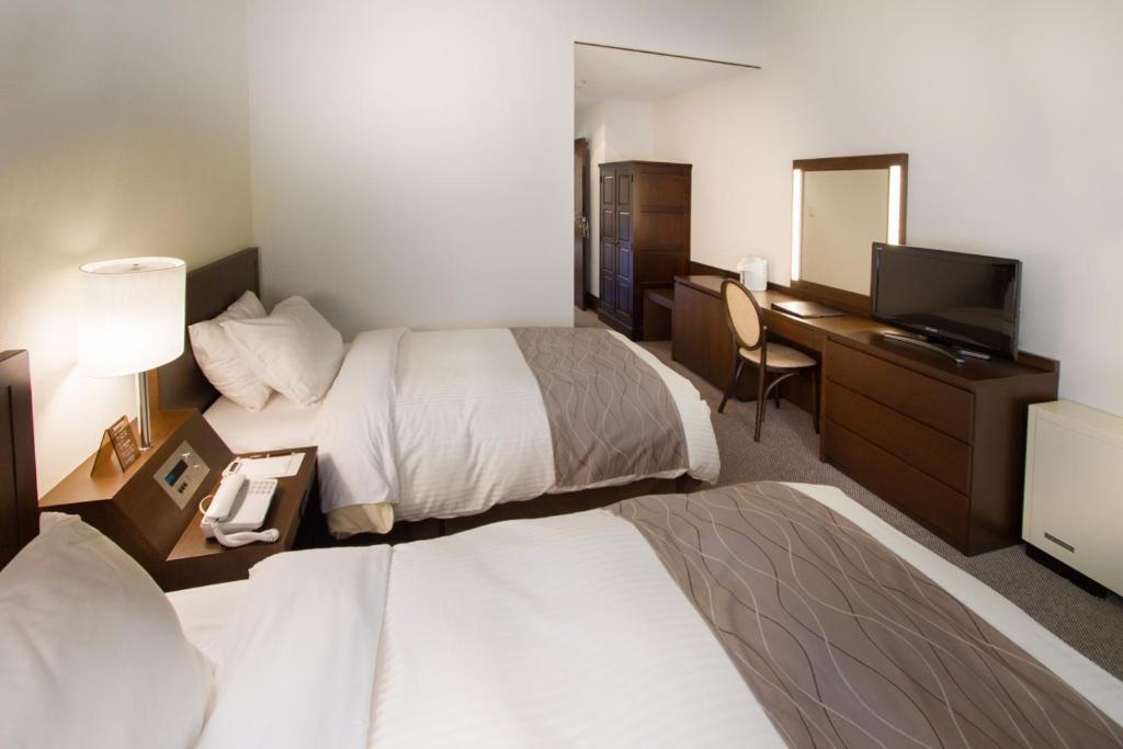 Minamimaki八岳高原酒店的酒店客房设有两张床、一张桌子和一台电视。
