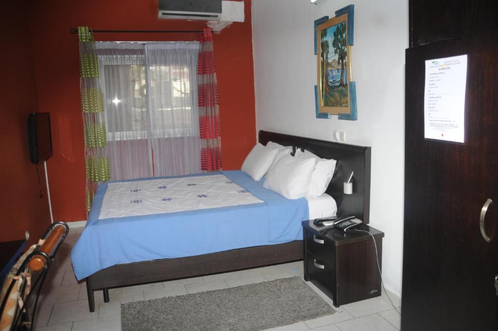 阿比让住宿旅游酒店的一间卧室配有一张带蓝色床单的床和一扇窗户。