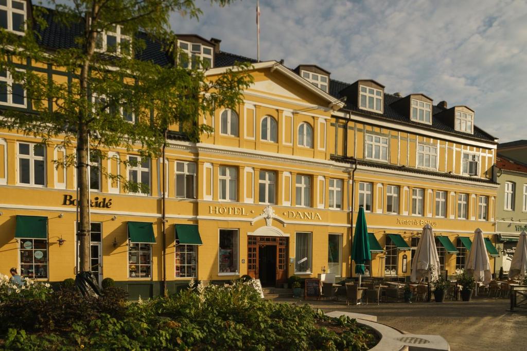 锡尔克堡达尼亚酒店的前面有桌子和遮阳伞的黄色建筑