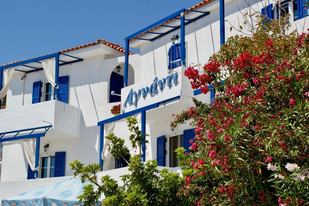 DiakoftiAgnadi Blue Apartments的白色的建筑,有蓝色的窗户,还有一棵红花树