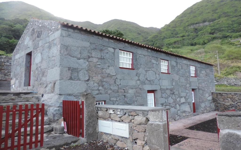 Fajã dos VimesCasas Dos Vimes的一座石头房子,后面有红色的大门和山脉