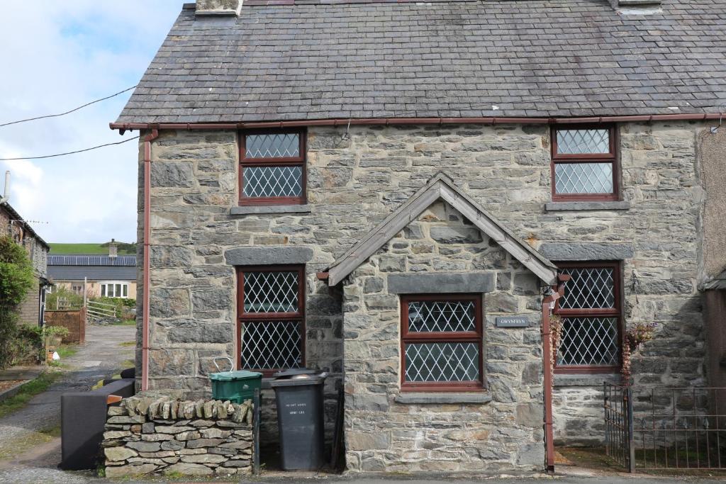 Cerrig-y-DruidionGwynfryn的一座古老的石头房子,有三个窗户和垃圾桶