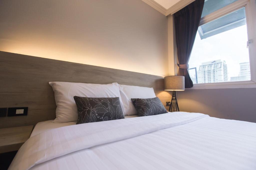 曼谷美心酒店的卧室配有带枕头的白色床和窗户。