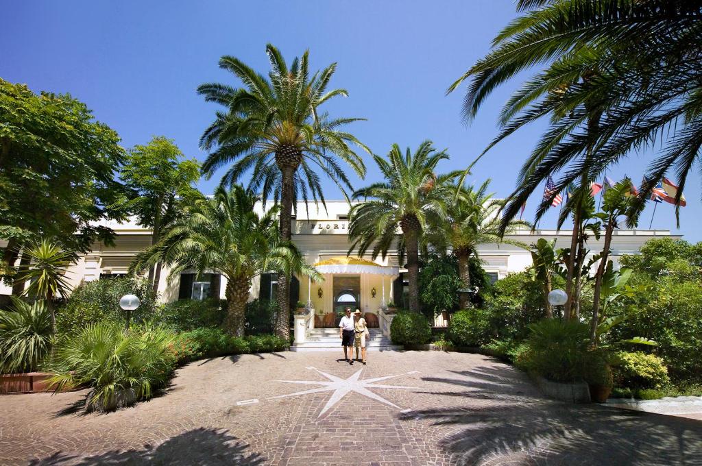 伊斯基亚弗拉里蒂尔那泰尔梅酒店的两个人站在一座棕榈树建筑前