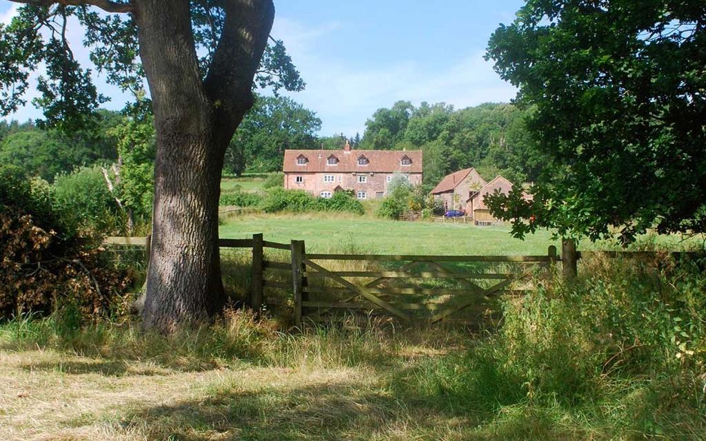 NewnhamGrove Farm B&B的田野上有栅栏和一棵树,有房子