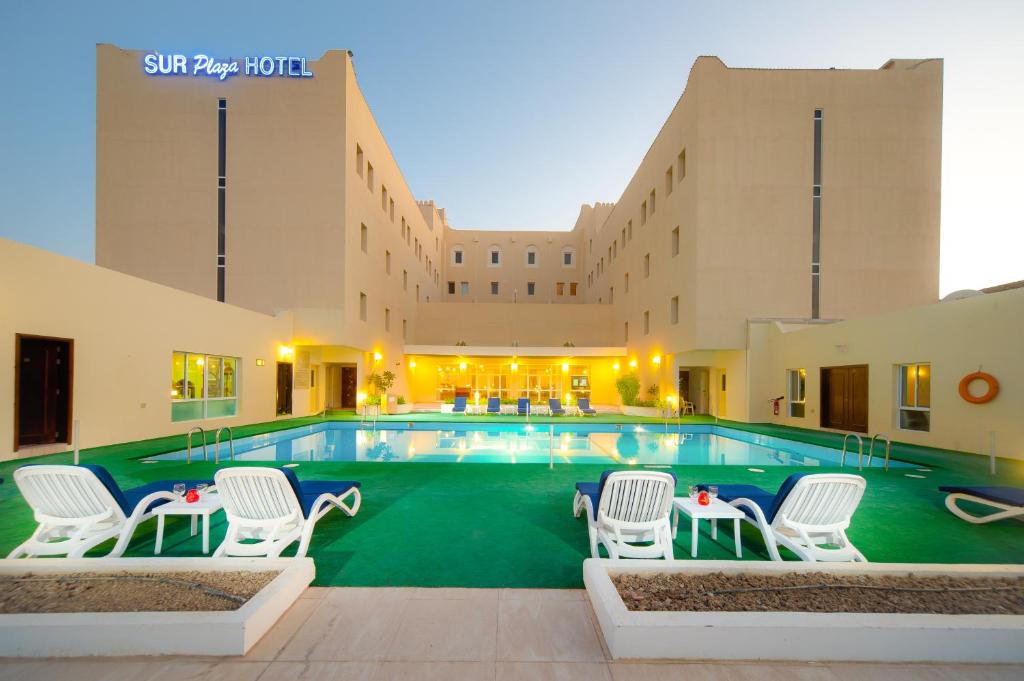 苏尔Sur Plaza Hotel的一座带白色椅子的酒店游泳池以及一座建筑