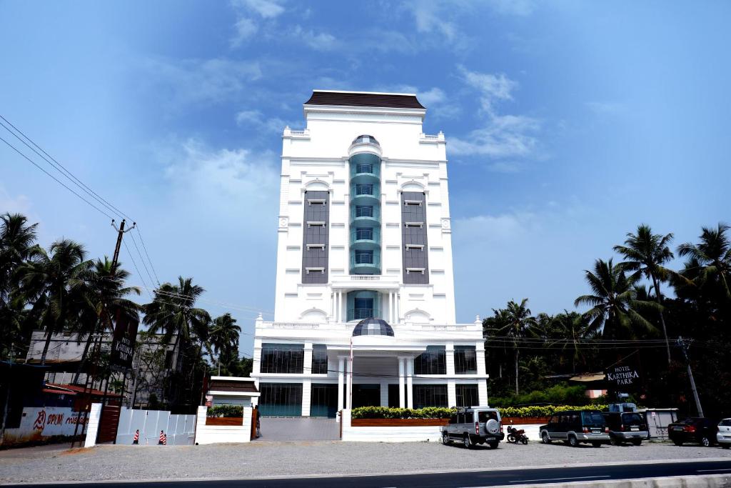 KazhakuttamHotel Karthika Park的一座高大的白色建筑,前面有汽车停放