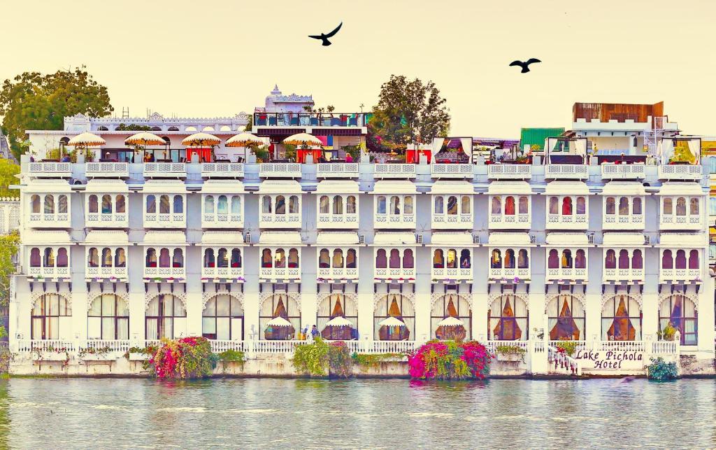 乌代浦Lake Pichola Hotel的一座白色的大建筑,鸟儿飞过水面