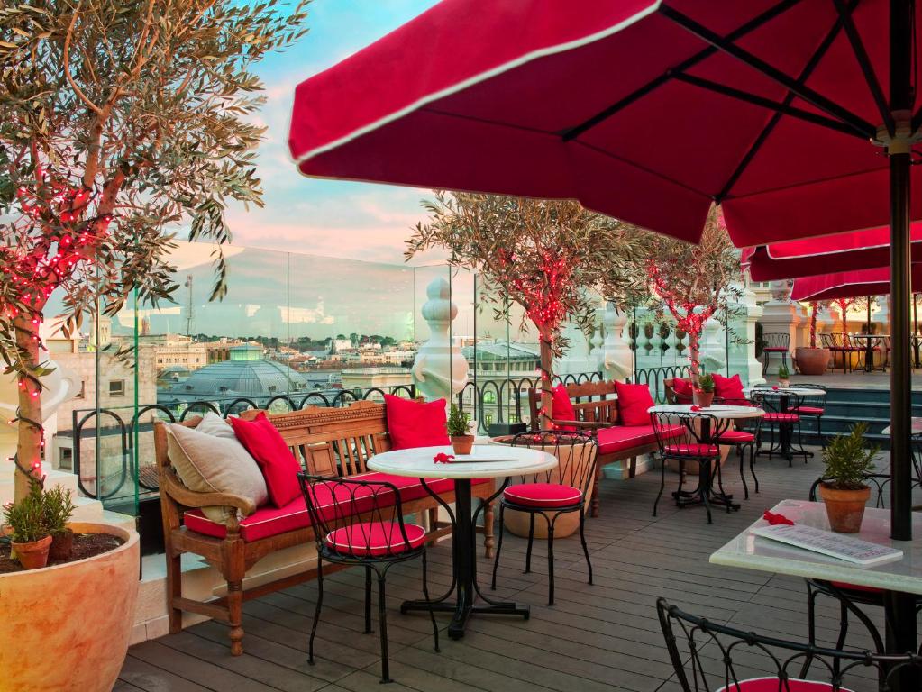 马德里The Principal Madrid, Small Luxury Hotels的一个带桌椅和红色遮阳伞的庭院