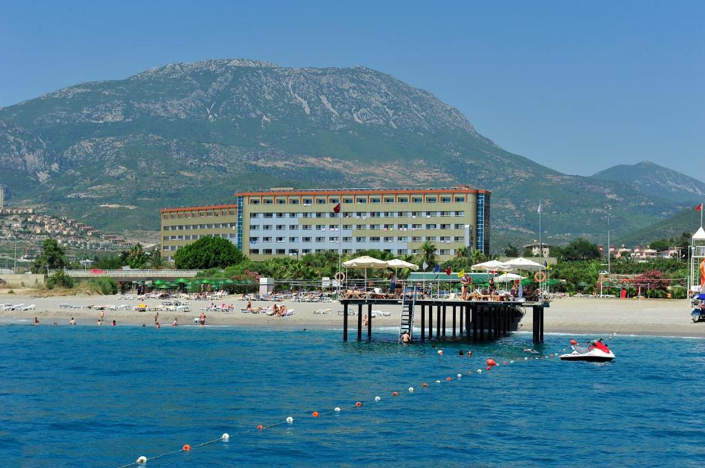 卡吉柯克Kırbıyık Resort Hotel - Alanya的水中的一个码头,有海滩和建筑