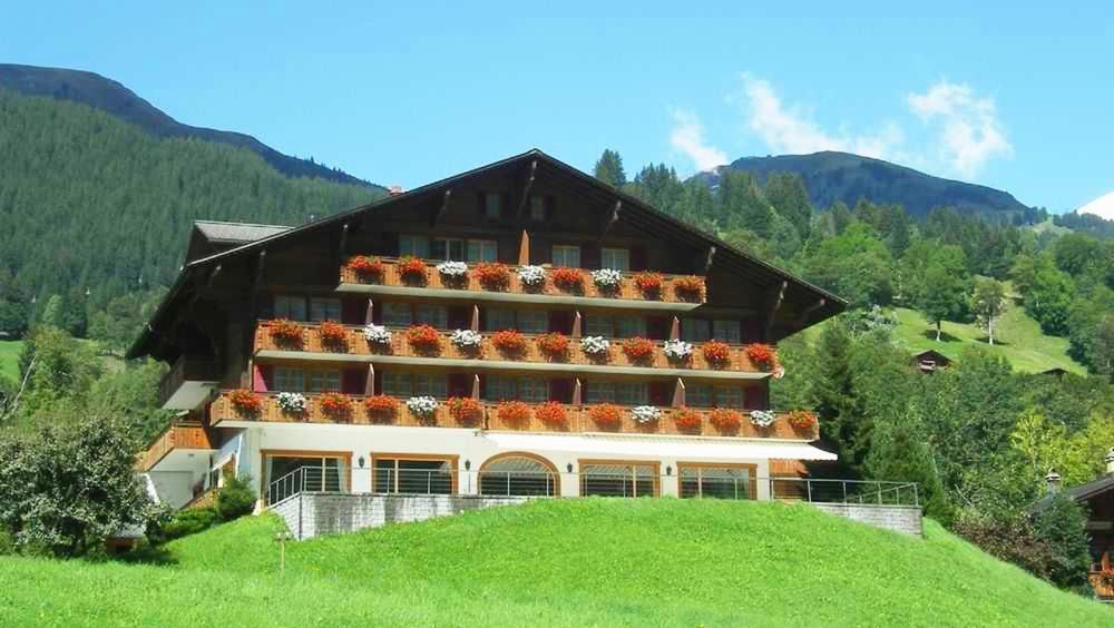 格林德尔瓦尔德Hotel Gletscherblick Grindelwald的绿色山顶上的大型建筑