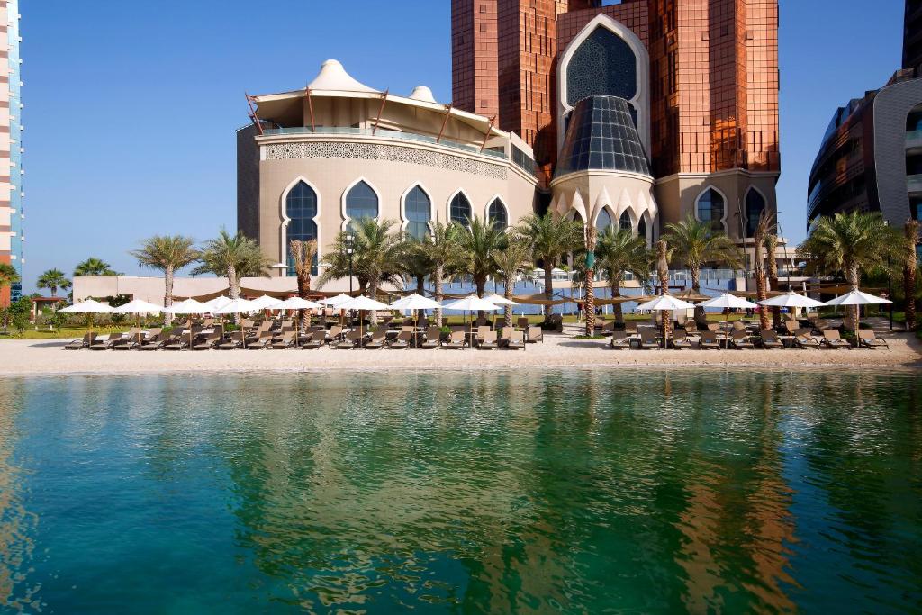 阿布扎比巴布皇宫公寓式酒店的水体旁的一座带椅子和遮阳伞的建筑