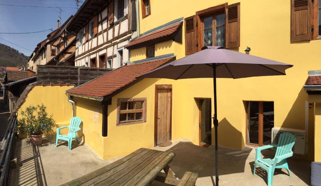 利克维Gîte Elisa et Léna的一座黄色的建筑,配有遮阳伞和两把椅子
