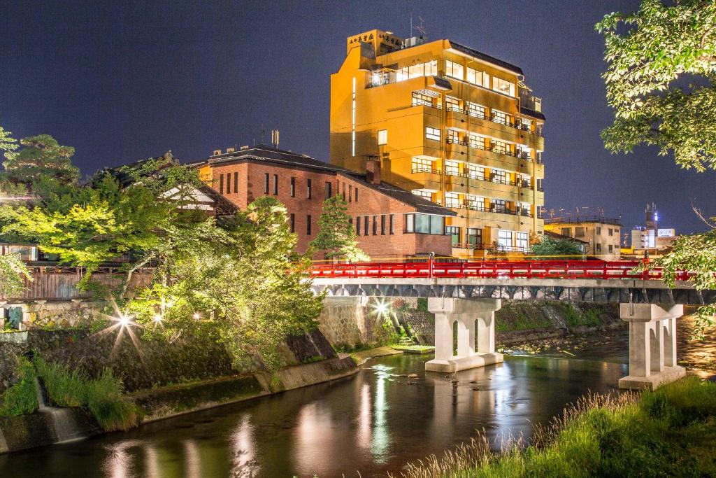 高山本阵平野福楼酒店的一条红色的火车穿过一条河上的桥梁