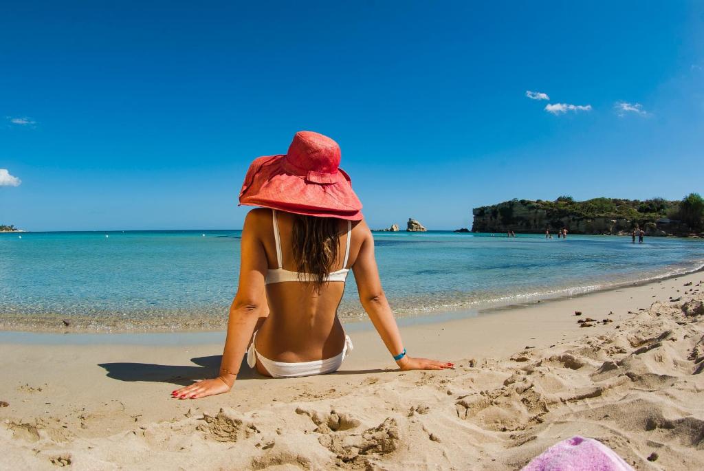 冯塔尼比安奇Futura Club Spiagge Bianche的坐在海滩上的戴帽子的女人