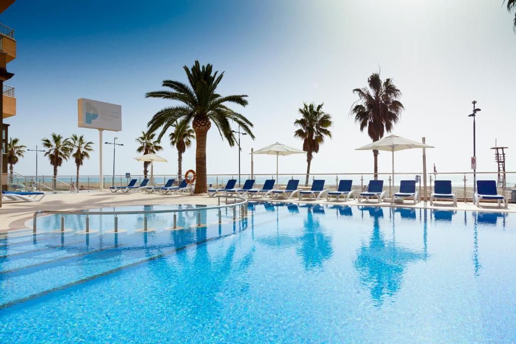 佩尼斯科拉本尼斯科拉宫酒店的一个带椅子和棕榈树的游泳池以及大海