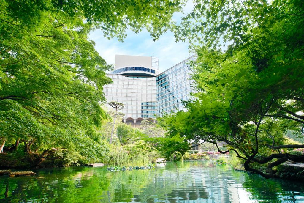 东京Hotel New Otani Tokyo The Main的树木公园和建筑物中的河流