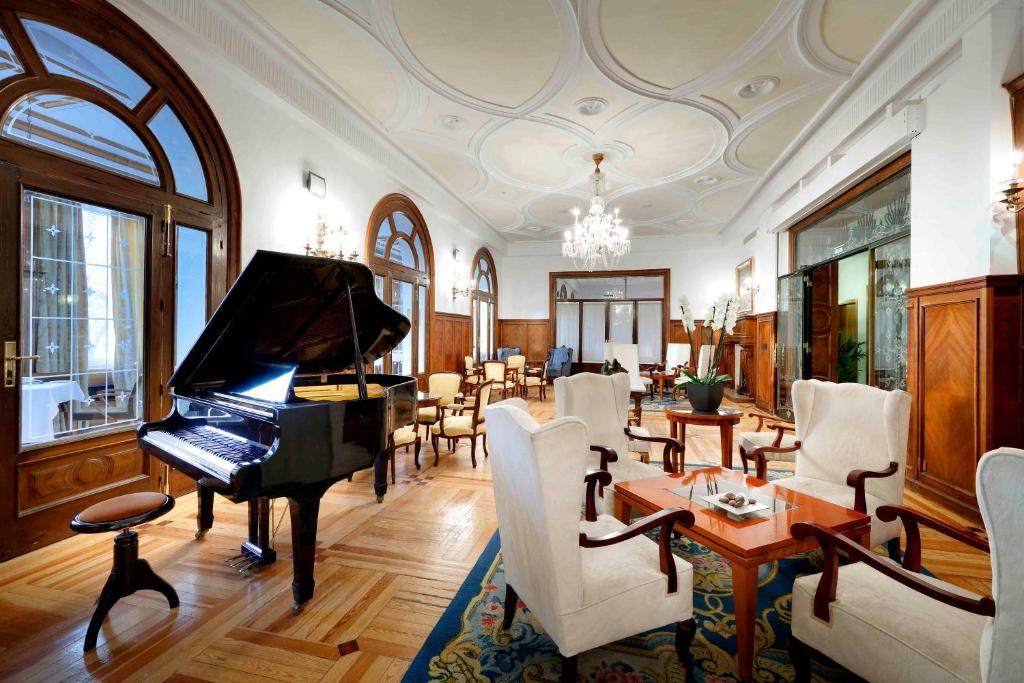 圣洛伦索-德埃斯科里亚尔埃克维多利亚酒店的一间带钢琴的客厅和一间餐厅