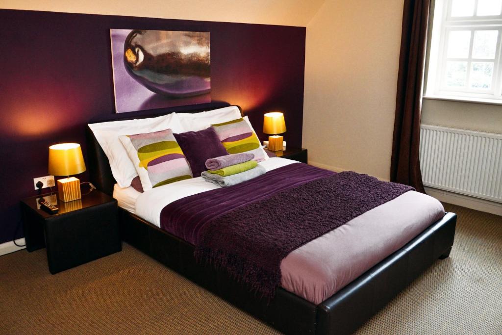 布由德利皇家森林乡村酒店的一间卧室配有一张大床,提供紫色和黄色枕头