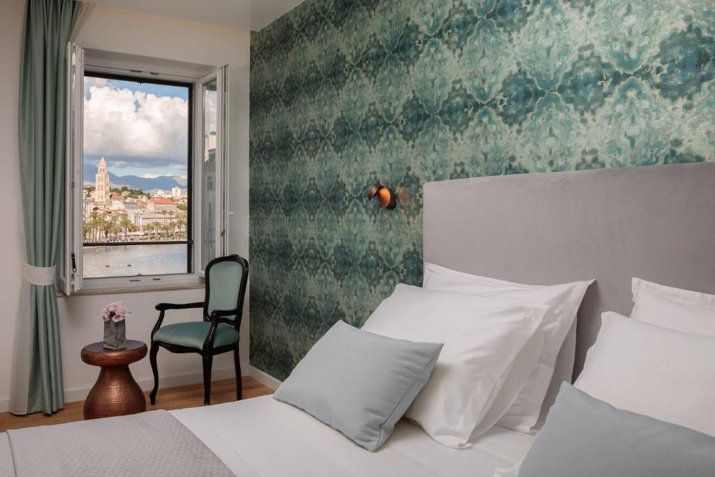 斯普利特Belvedere Luxury Rooms - Breathtaking View的一间卧室设有一张床、一个窗口和一把椅子