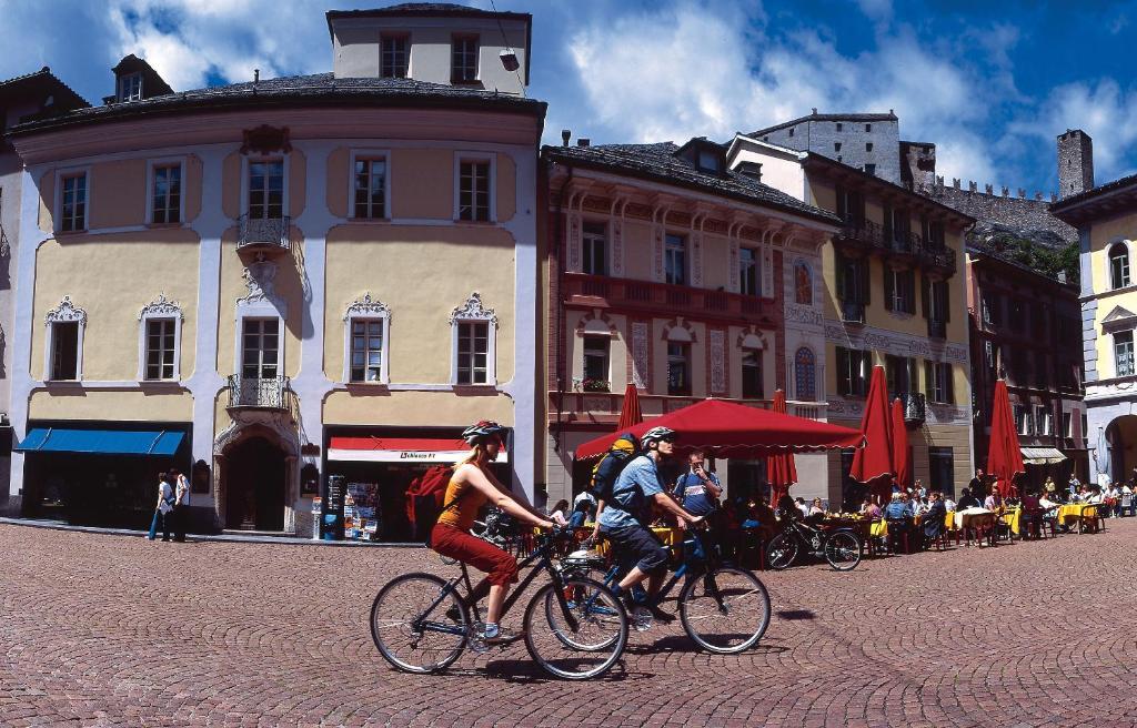 贝林佐拉Bellinzona Piazza Collegiata的两人骑车在城市街道上
